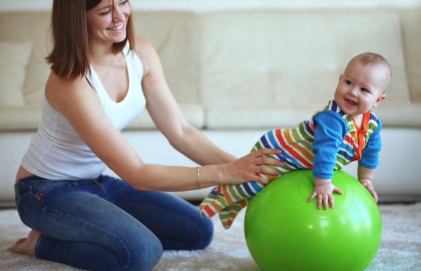 Mamá estimulando los sentidos de su bebé con una pelota verde de pilates
