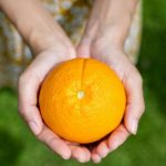 "manos sosteniendo una naranja"